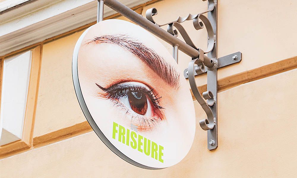 Haidhausen: das runde Nasenschild an der Fassade mit einem Auge und dem Schriftzug Friseure.